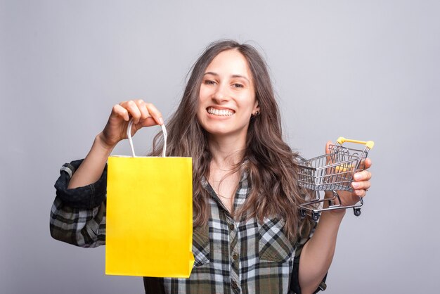 Foto retrato de mujer joven sonriente con carrito y bolsa de compras.