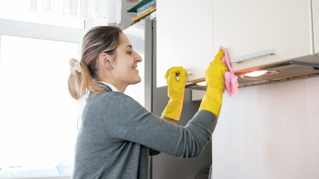 Retrato de mujer joven sonriente feliz limpiando y puliendo superficies en la cocina mientras hace las tareas del hogar.