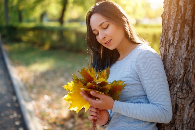 Retrato de mujer joven sonriente con hojas de otoño delante de follaje