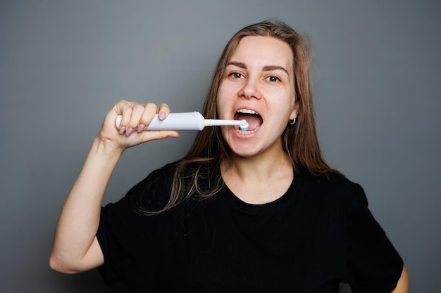 Retrato de una mujer joven sonriente sin maquillaje en una camiseta negra cepillándose los dientes mujer madura concepto de belleza natural Cepillo matutino para dientes cepillo ultrasónico dental