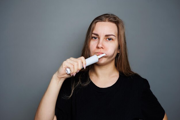 Retrato de una mujer joven sonriente sin maquillaje en una camiseta negra cepillándose los dientes mujer madura concepto de belleza natural Cepillo matutino para dientes cepillo ultrasónico dental