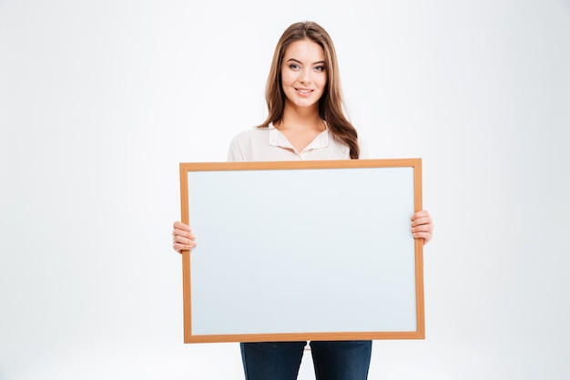 Retrato de una mujer joven sonriente mostrando tablero en blanco aislado en una pared blanca