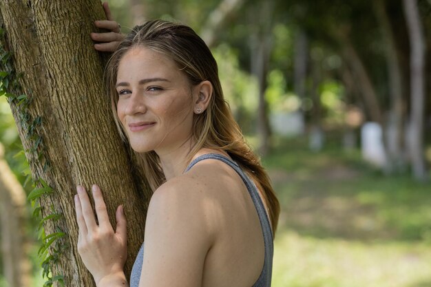 Foto retrato de una mujer joven sonriente en un parque en un hermoso día soleado mujer abrazando un árbol fondo verde y naturaleza foto de alta calidad