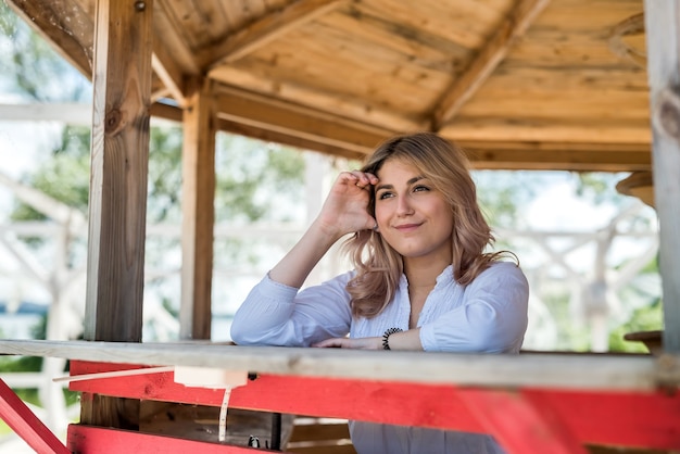 Retrato de mujer joven sonriente que disfruta del tiempo de vacaciones, cerca de la playa de arena en la glorieta de madera.