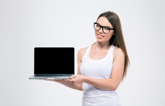 Retrato de una mujer joven sonriente que muestra la pantalla del portátil en blanco aislada