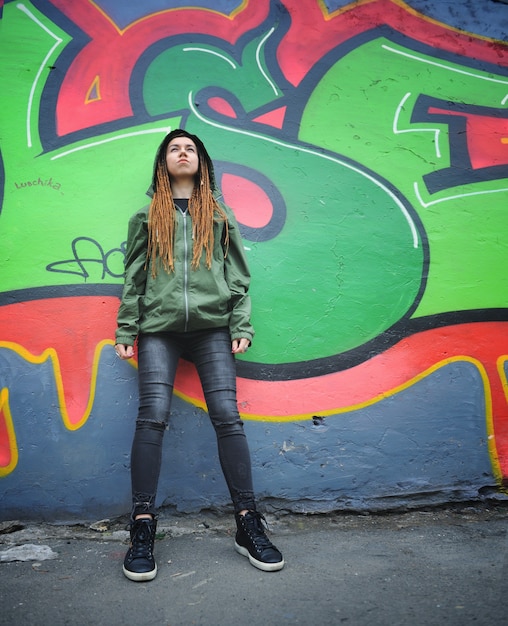 Foto retrato de mujer joven sonriente con rastas, contra graffiti