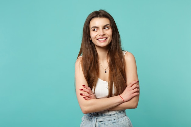 Retrato de mujer joven sonriente en ropa casual ligera mirando a un lado cogidos de la mano cruzados aislados sobre fondo de pared azul turquesa. Concepto de estilo de vida de emociones sinceras de personas. Simulacros de espacio de copia.