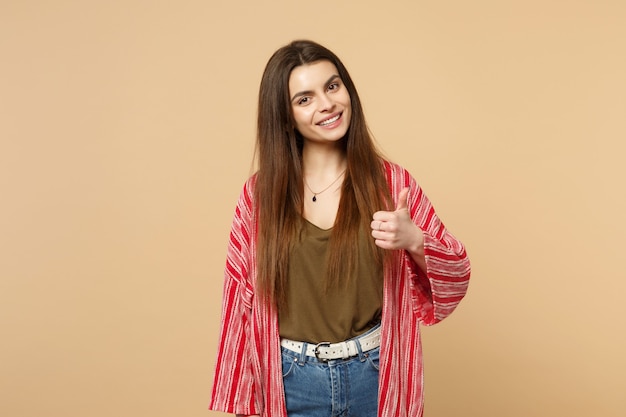 Retrato de mujer joven sonriente en ropa casual mirando a cámara, mostrando el pulgar hacia arriba aislado sobre fondo de pared beige pastel en estudio. Personas sinceras emociones, concepto de estilo de vida. Simulacros de espacio de copia.