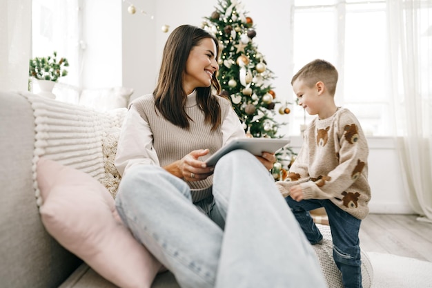 Retrato de una mujer joven sonriente con su hijo con tableta digital en las vacaciones de invierno en casa