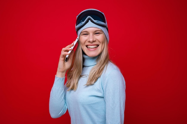 Retrato de una mujer joven sonriente en un suéter y gafas de esquí hablando por teléfono