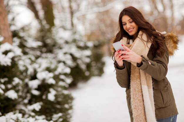 Retrato de mujer joven sonriente con teléfono celular en invierno al aire libre