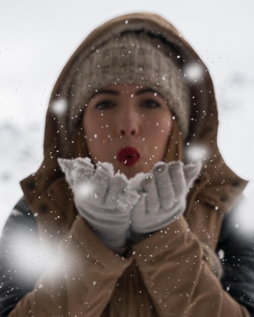 Foto retrato de una mujer joven soplando un beso durante la nieve