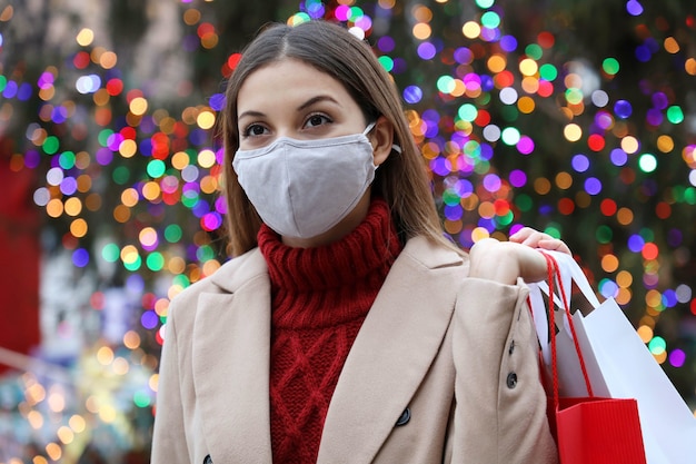 Retrato de mujer joven sosteniendo bolsas de compras caminando en las calles de la ciudad con árbol de luces de Navidad