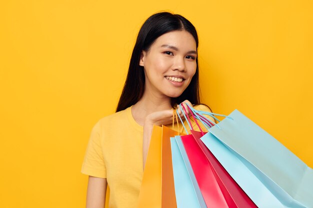 Retrato de una mujer joven sosteniendo bolsas de compras contra un fondo amarillo