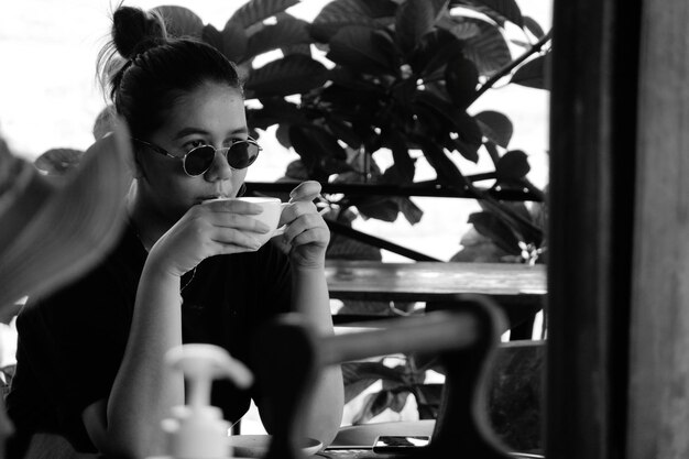 Foto retrato de una mujer joven sosteniendo un café mientras está sentada en la ventana