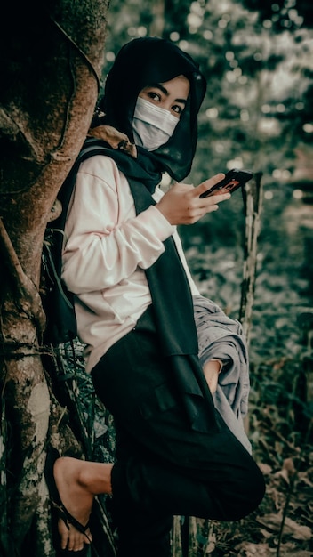 Foto retrato de una mujer joven sosteniendo una cámara mientras está de pie en un árbol