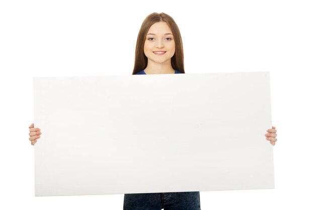 Foto retrato de una mujer joven sosteniendo un cartel en blanco contra un fondo blanco