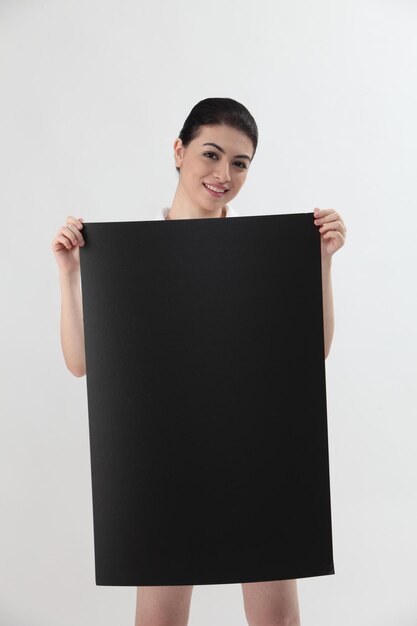 Foto retrato de una mujer joven sosteniendo un cartel negro en blanco contra un fondo gris