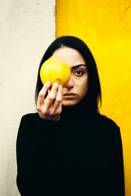 Retrato de una mujer joven sosteniendo frutas contra la pared