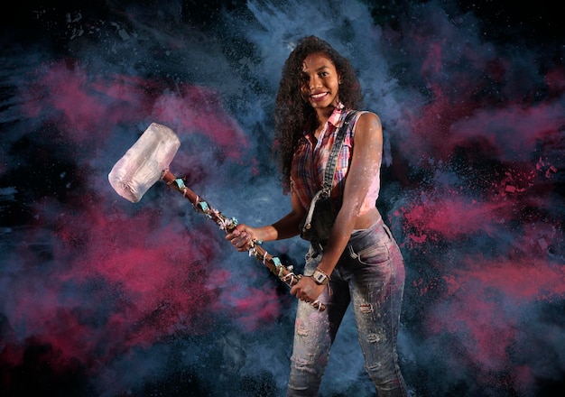 Foto retrato de una mujer joven sosteniendo un martillo mientras está de pie contra un fondo de color