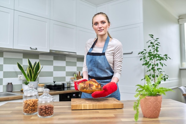 Retrato de mujer joven sosteniendo pollo al horno mirando a la cámara