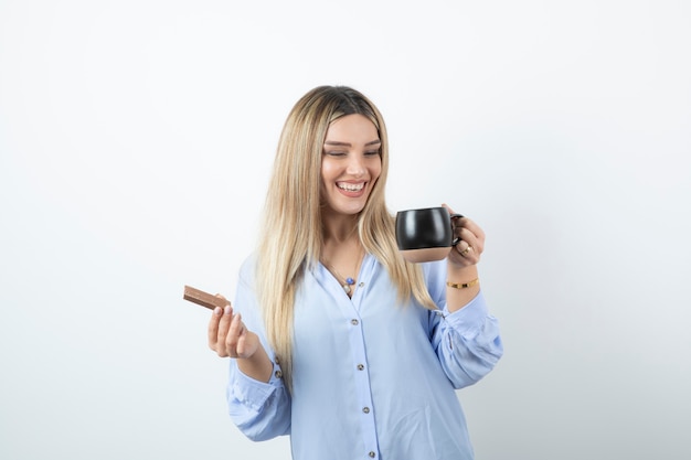 Retrato de mujer joven sosteniendo una taza de bebida caliente con barra de chocolate