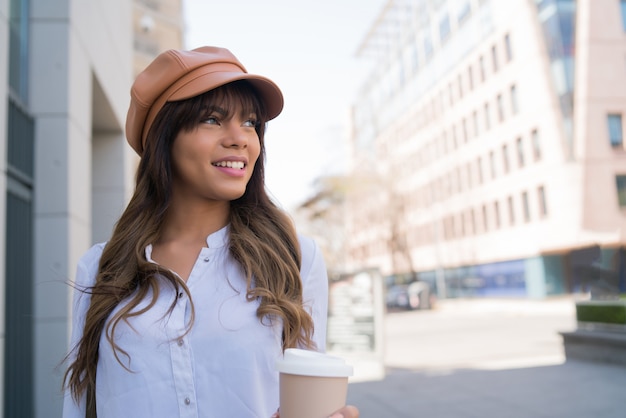 Retrato de mujer joven sosteniendo una taza de café mientras camina al aire libre en la calle