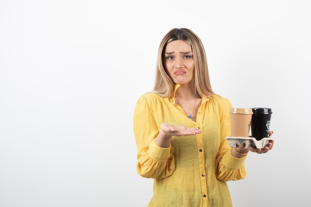 Retrato de mujer joven sosteniendo tazas de café y sin saber qué hacer.