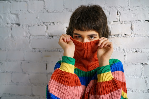 Retrato de una mujer joven con un suéter multicolor, cubriendo su rostro con un suéter. El concepto de timidez