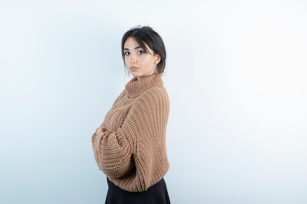 Retrato de mujer joven en suéter de punto posando en la pared blanca