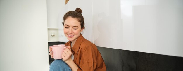 Foto retrato de una mujer joven con una taza de café sentada en la cocina y bebiendo una bebida aromática en casa