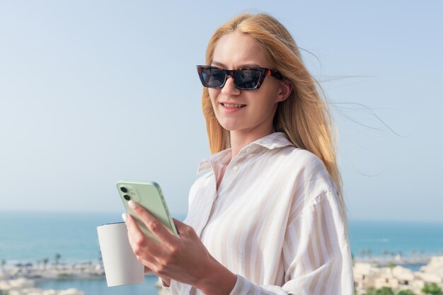 Retrato de una mujer joven con una taza de café y un teléfono durante las vacaciones de verano