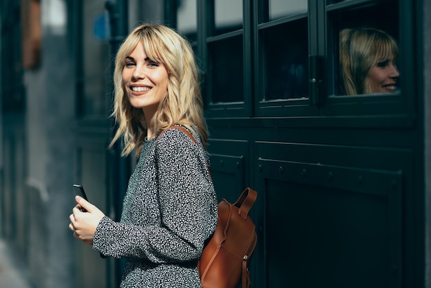 Retrato de una mujer joven con un teléfono inteligente mientras está de pie contra el edificio