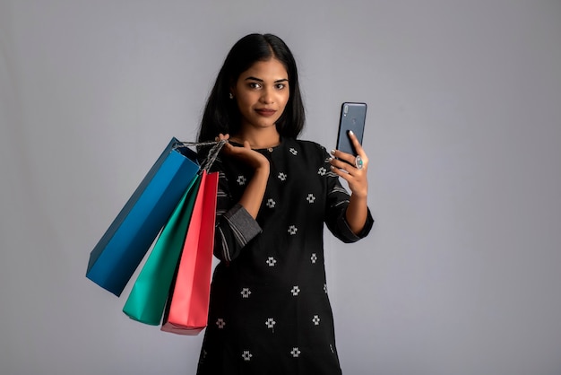 Retrato de una mujer joven mediante teléfono móvil con bolsas de compras en sus manos.