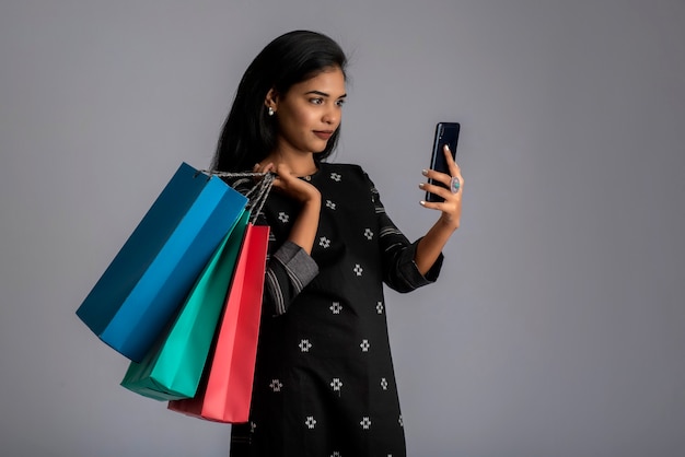 Retrato de una mujer joven mediante teléfono móvil con bolsas de compras en sus manos.