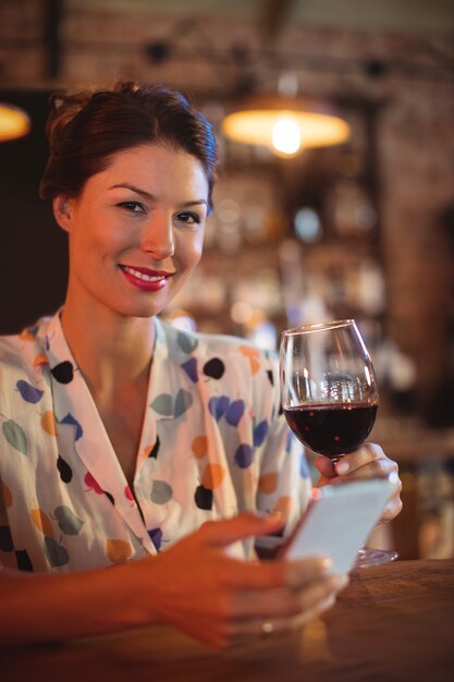 Foto retrato de mujer joven mediante teléfono móvil mientras toma vino