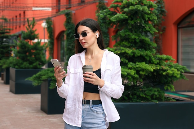 Retrato de una mujer joven con un teléfono y una taza de café en el patio de la oficina