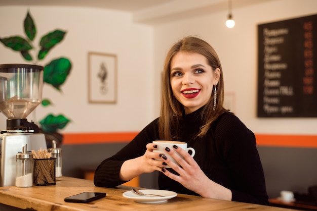 Retrato de mujer joven tomando café en la cafetería.