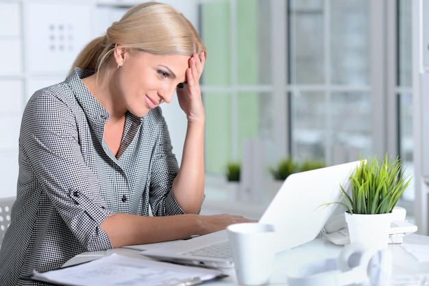 retrato, de, mujer joven, trabajando, con, computador portatil, en, oficina