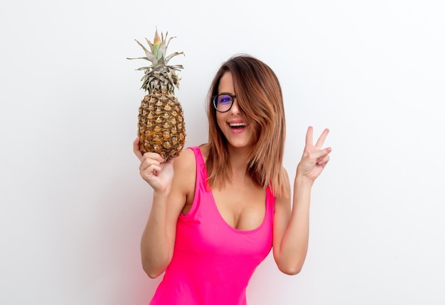 Retrato de mujer joven en traje de baño y anteojos con piña sobre fondo blanco. Concepto de imagen de temporada de verano