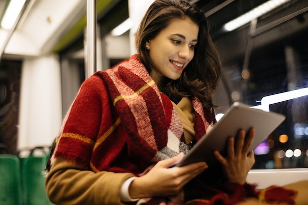 Retrato de una mujer joven en el transporte público, sentado y usando su tableta en el moderno tranvía.