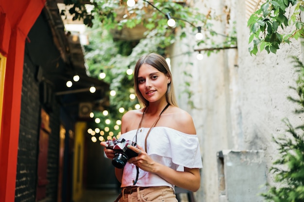 Retrato de mujer joven turista apasionado con cámara retro en sus manos mientras posa en la arquitectura antigua urbana. Descubrir nuevos lugares