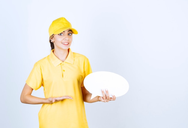 Retrato de una mujer joven en uniforme amarillo sosteniendo un bocadillo de diálogo en blanco vacío.