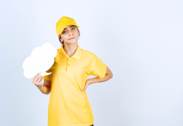 Retrato de una mujer joven en uniforme amarillo sosteniendo una nube de burbujas de discurso blanco vacío.
