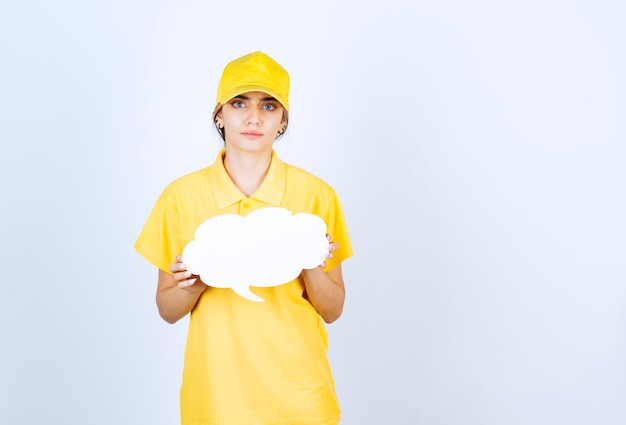 Retrato de una mujer joven en uniforme amarillo sosteniendo una nube de burbujas de discurso blanco vacío.