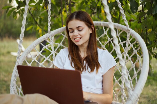 Foto retrato de una mujer joven usando una computadora portátil mientras está sentada en el parque