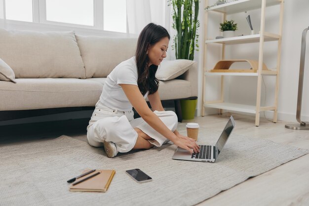 Foto retrato de una mujer joven usando una computadora portátil mientras está sentada en el sofá en casa