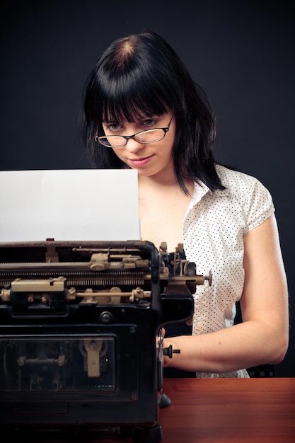 Retrato de una mujer joven usando una máquina de escribir contra un fondo negro