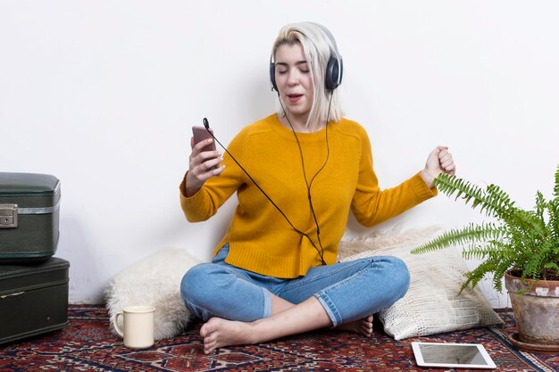 Foto retrato de una mujer joven usando un teléfono móvil mientras está sentada contra un fondo blanco