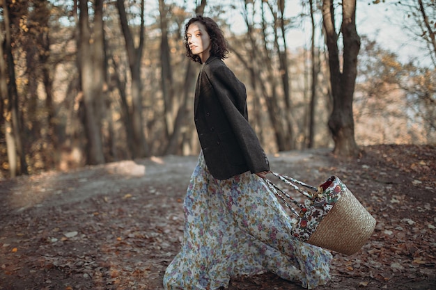 Retrato de mujer joven vestida vintage con cesta de flores caminando en el parque de otoño